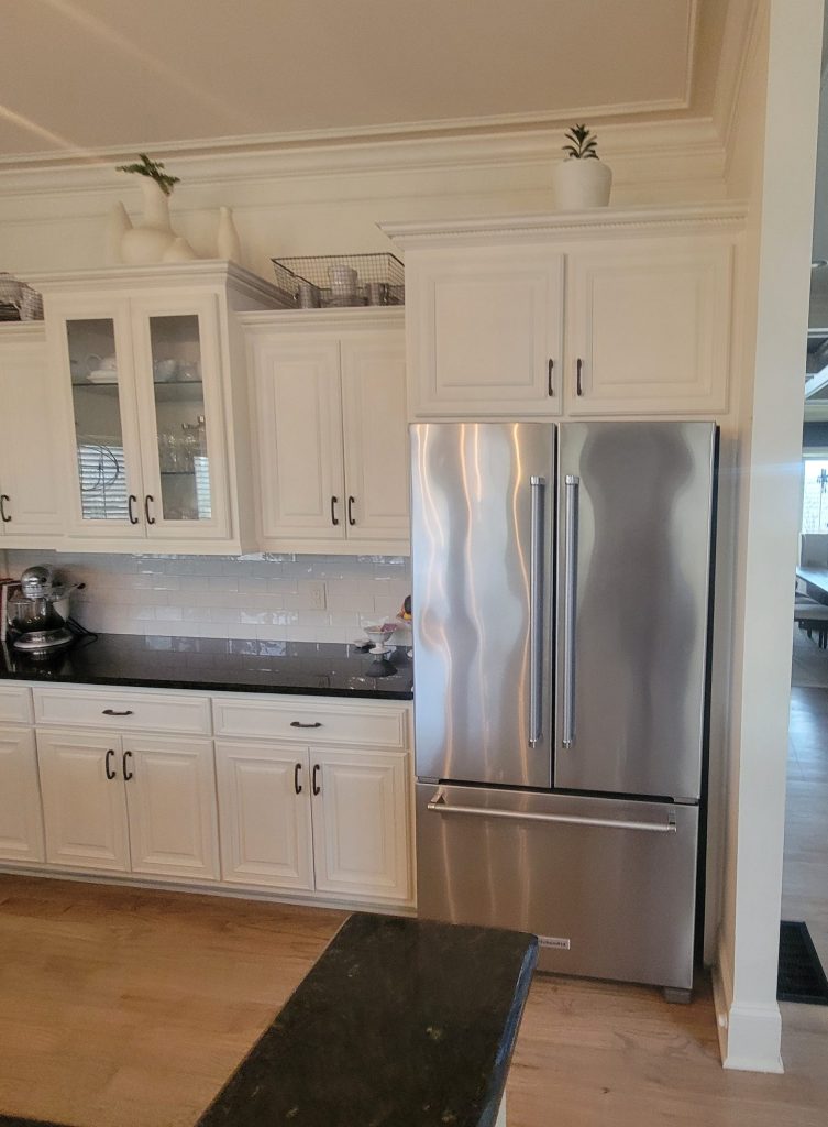 shot of kitchen with off white cabinets, black pulls, and a black countertop and gray fridge