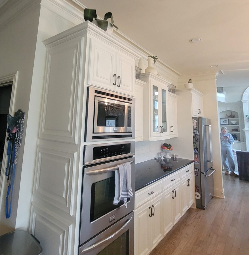 Angeled shot of kitchen with off white cabinets, black pulls, and a black countertop with inset microwave and oven