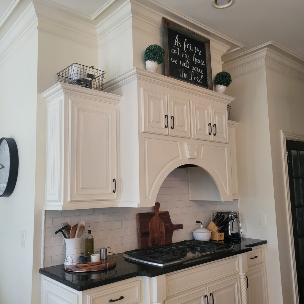 picture of kitchen range with off-white cabintery, black countertop, and stovetop range