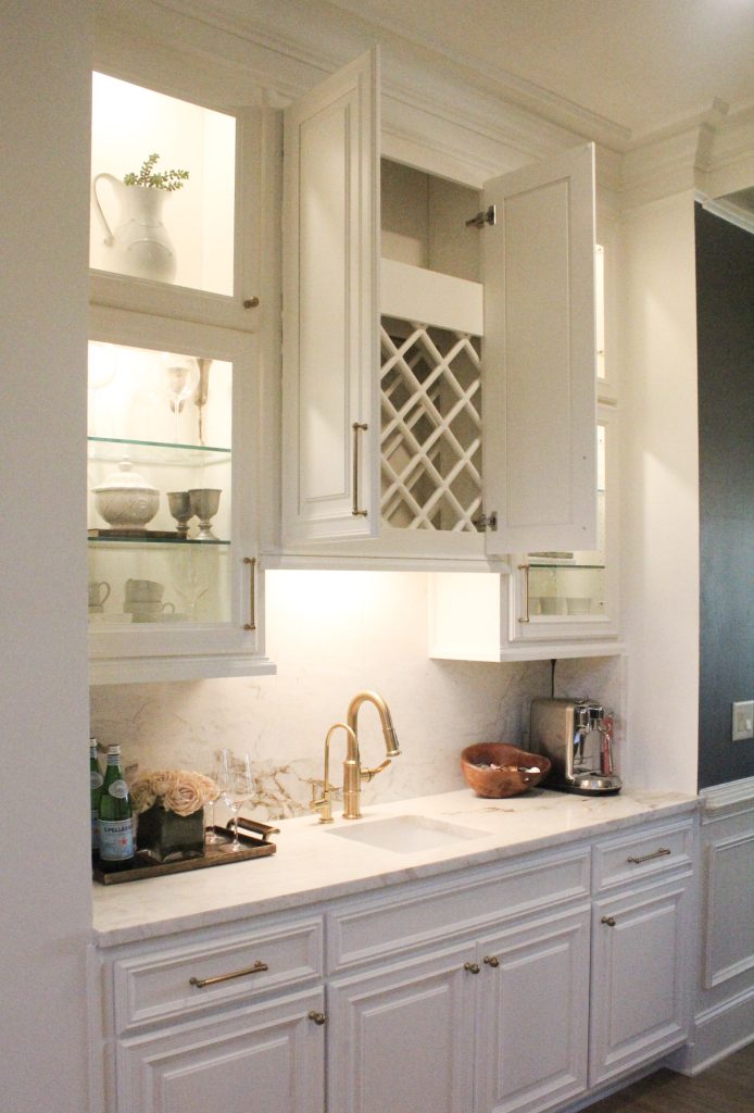 bright wet bar with white cabinets, gold knobs and faucet, under cabinet lighting and a white quartz countertop