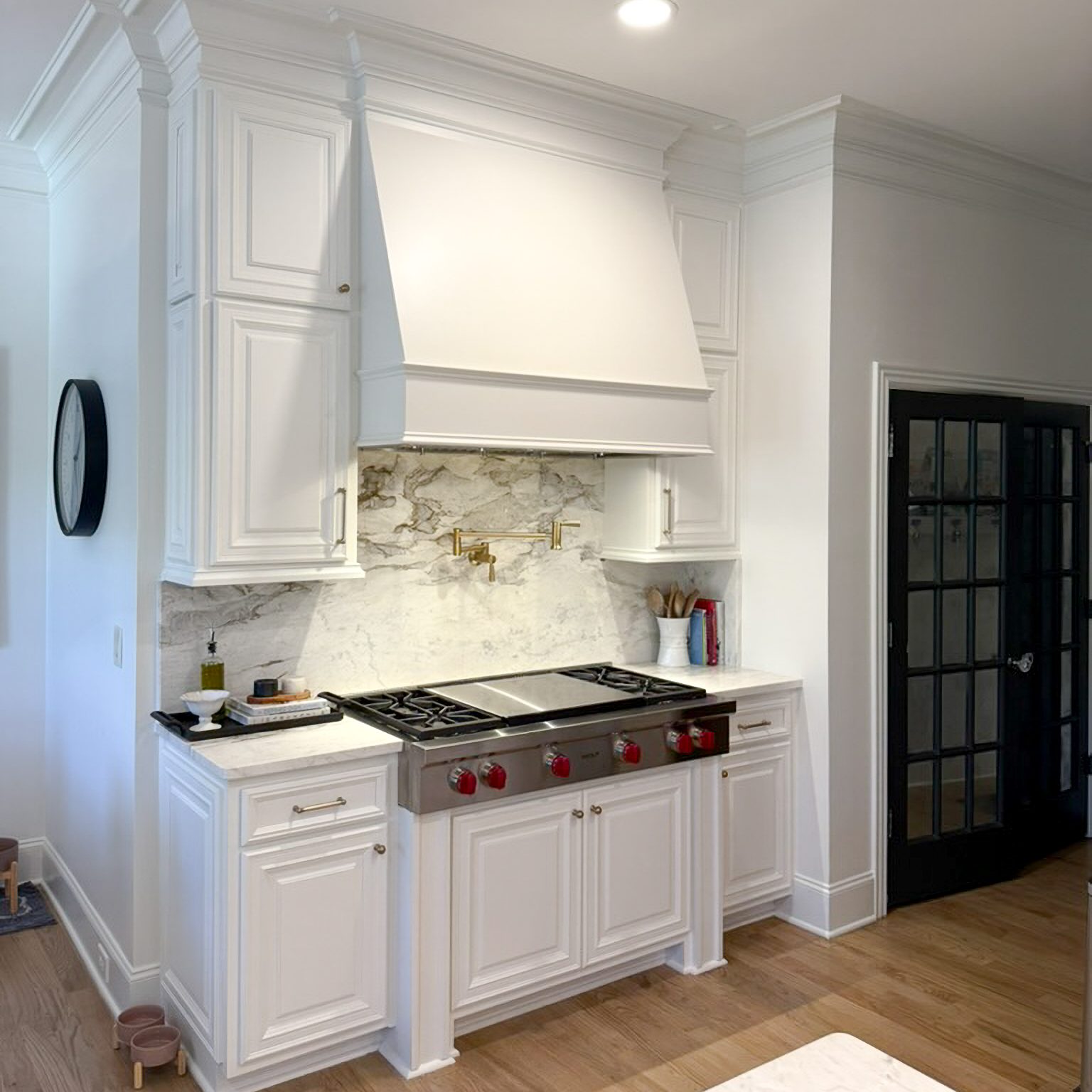image of kitchen range with bright white hood, white cabinetry, white and gold veined quartz countertop and backsplash, and stovetop range