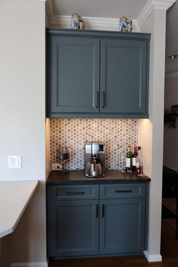 Vertical shot of wet bar with deep blue cabinets, hexagonal backsplash and dark countertops