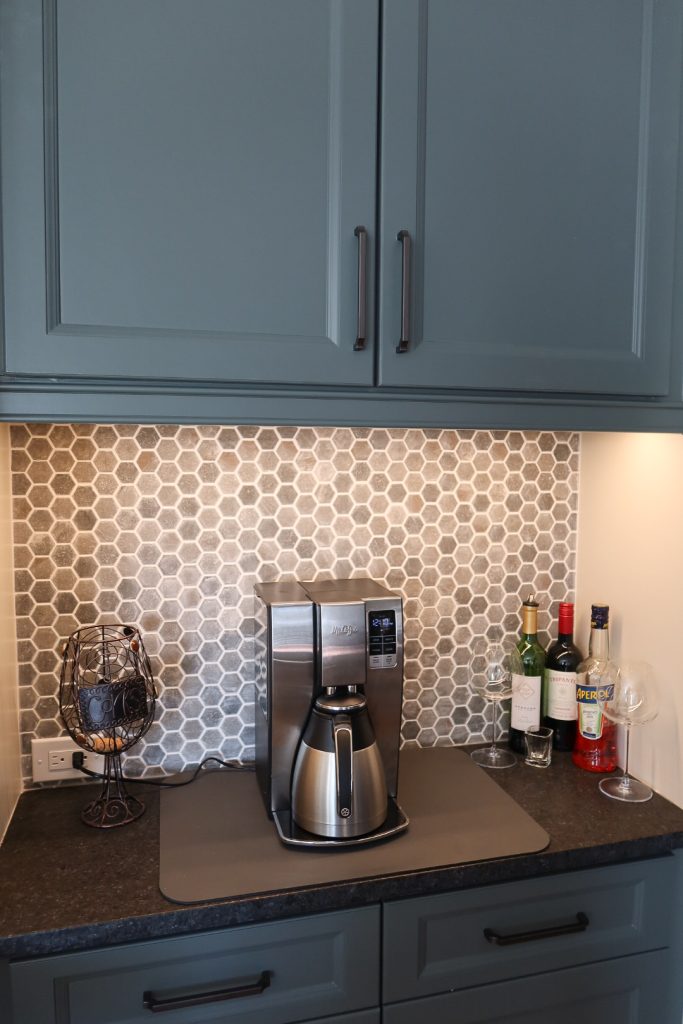 Vertical shot of wet bar with deep blue cabinets, hexagonal backsplash and dark countertops