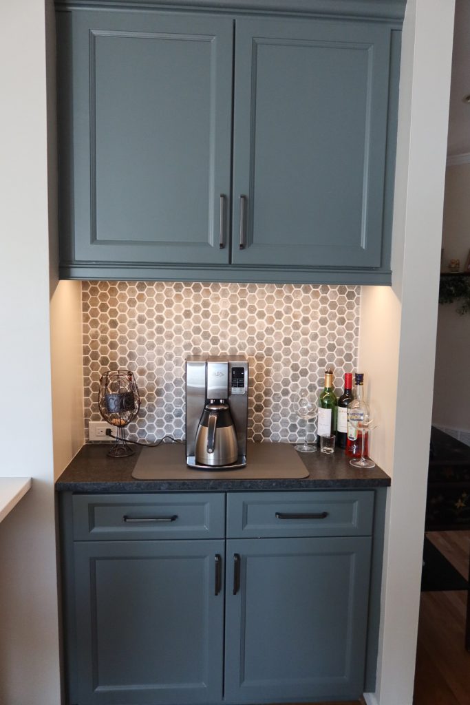Vertical shot of wet bar with deep blue cabinets, hexagonal backsplash and dark countertops