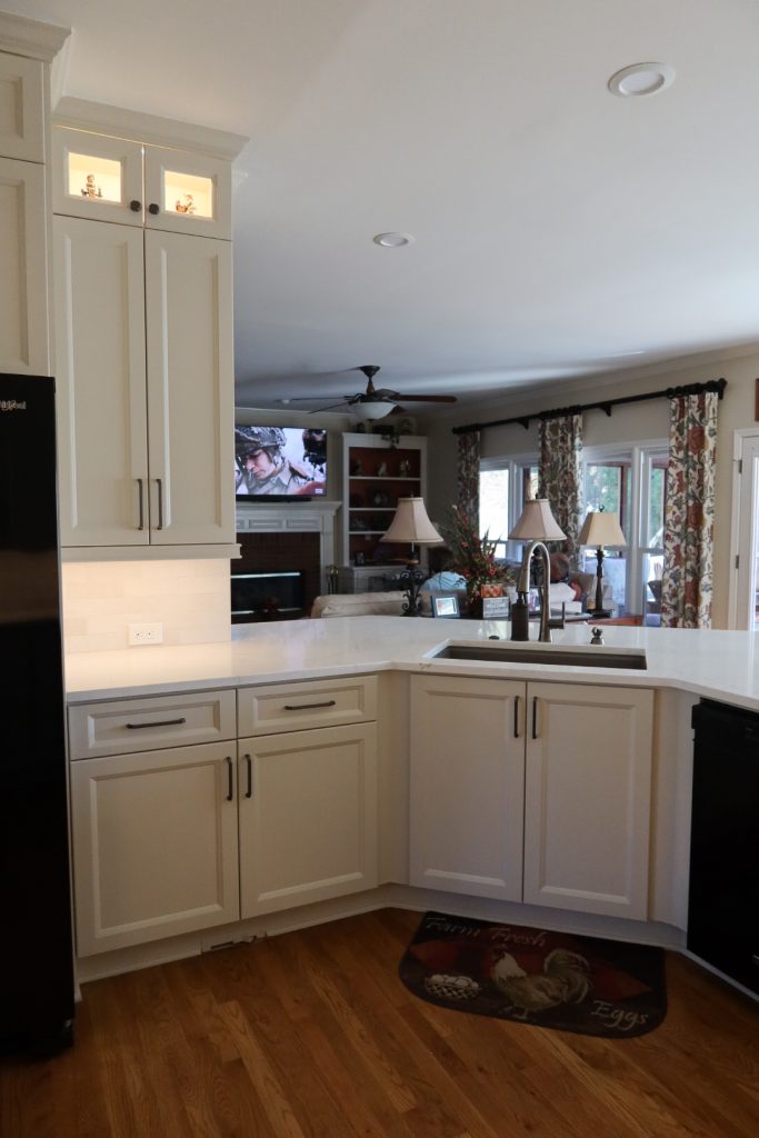 vertical shot of bright white kitchen with white countertops, cabinets and in-cabinet and under-cabinet lighting and black hardware
