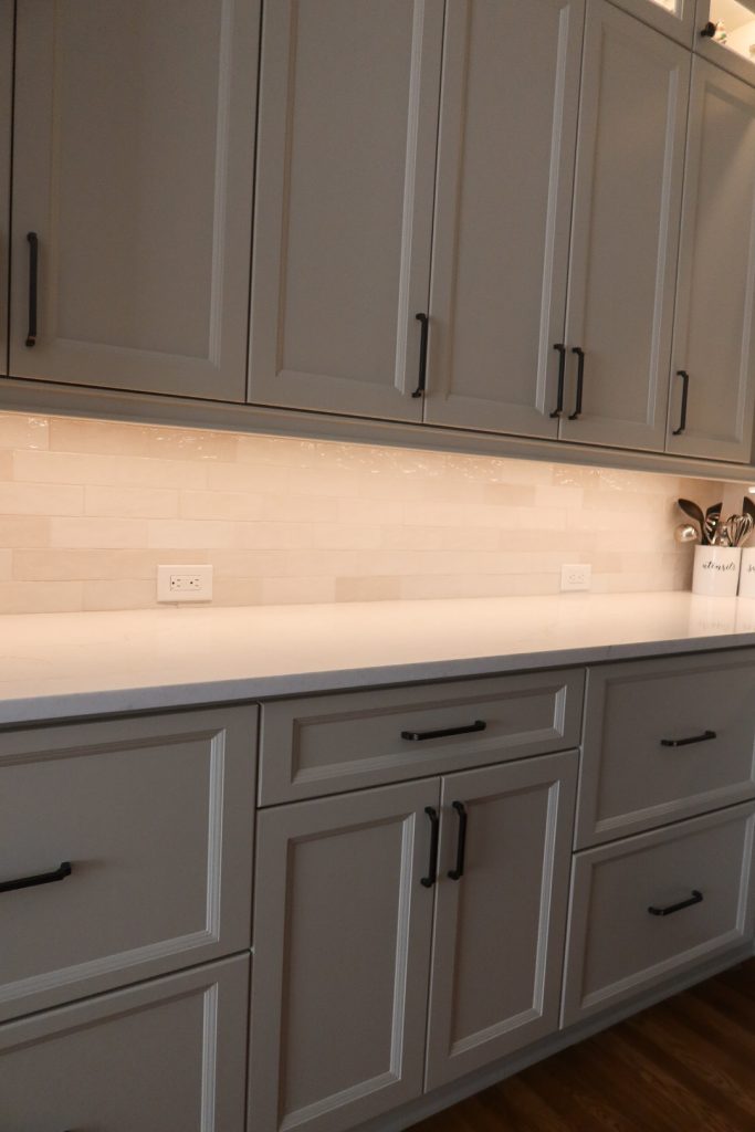 vertical shot of lit upper and lower off-white cabinets with white countertops
