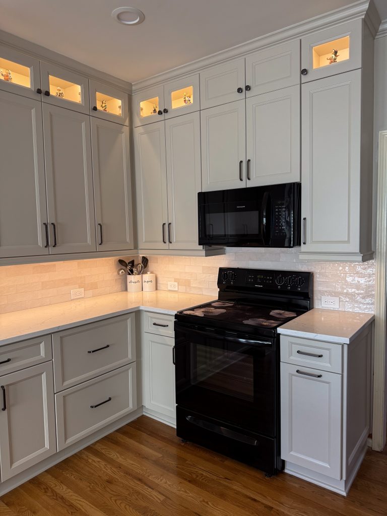 vertical shot of bright white kitchen with white countertops, cabinets and in-cabinet and under-cabinet lighting and black appliances
