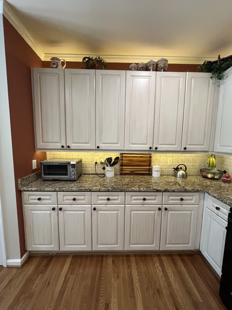vertical shot of a dated kitchen with white wood cabinets, granite countertop and burnt red walls