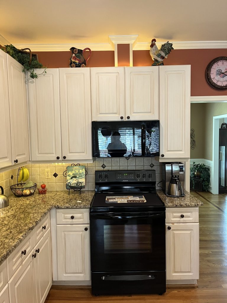 vertical shot of a dated kitchen with white wood cabinets, granite countertop and burnt red walls