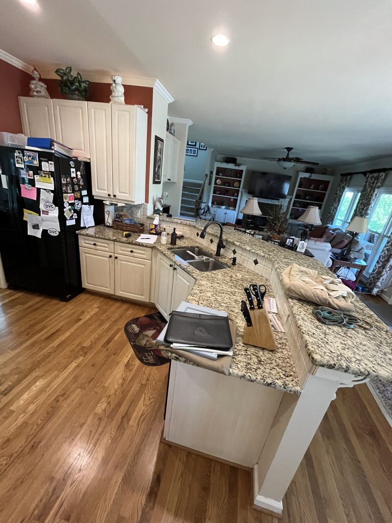 vertical shot of a dated kitchen with white wood cabinets, granite countertop, black fridge and burnt red walls and