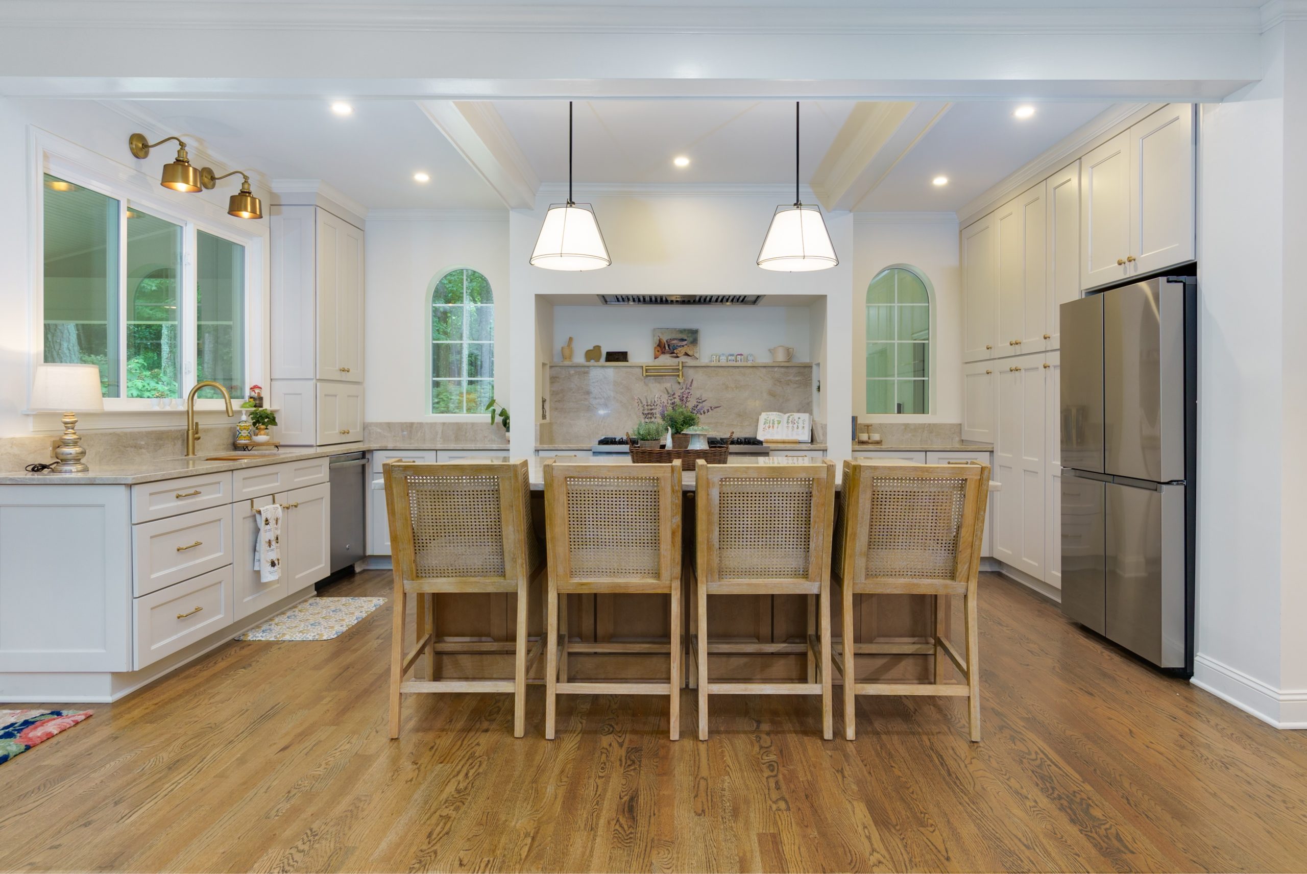 White Kitchen remodel with large island Remodeled white kitchen featuring custom cabinetry, a large center island with seating, pendant lights, stainless steel appliances, and hardwood floors.