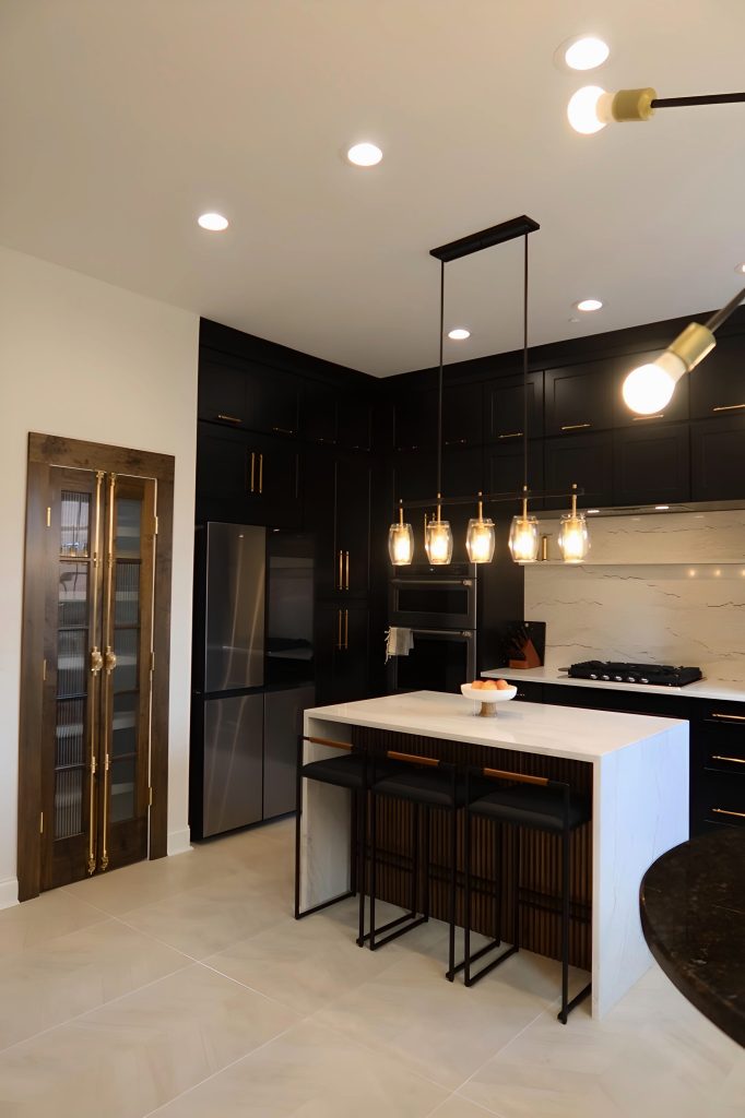 zoomed out photo of modern kitchen with black cabinetry, gold fixtures and white quartz throughout with wooden pantry door