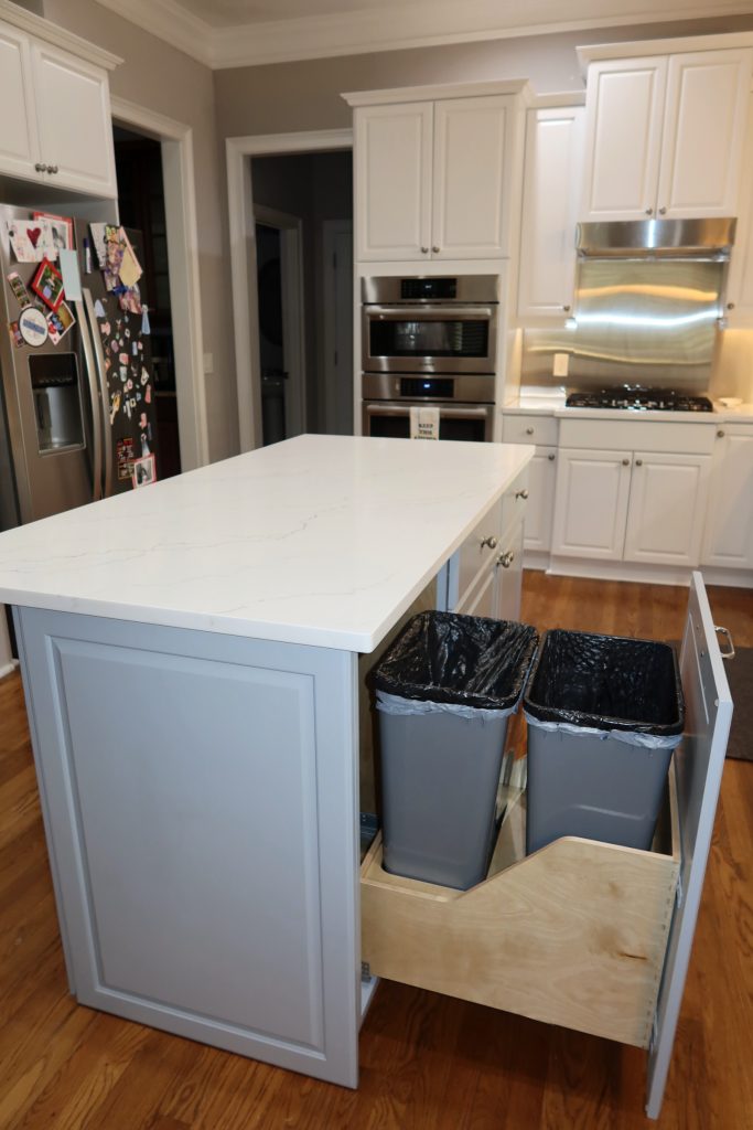 pull-out trash cans in a light blue remodeled island white white quartz countertop