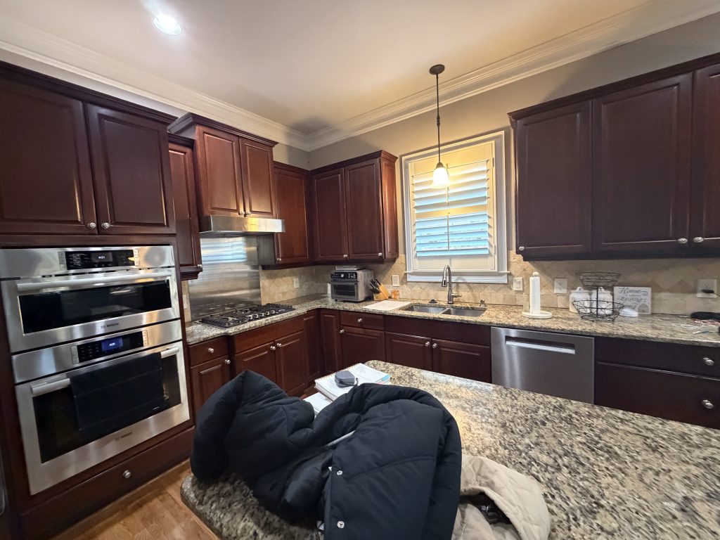 Kitchen before renovation with dark brown cabinets, granite countertops, and tile backsplash.