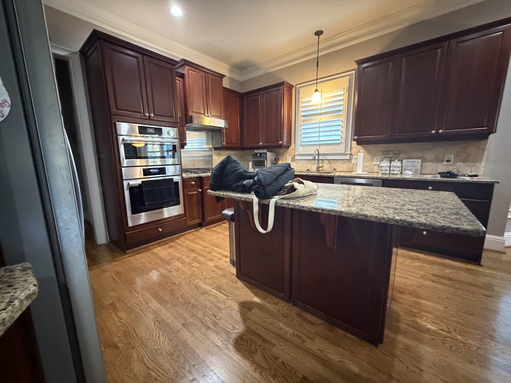 Kitchen before renovation with dark brown cabinets, granite countertops, and tile backsplash.