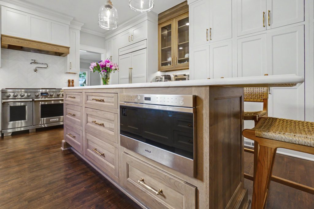Warm wood kitchen island with built-in Wolf microwave drawer and custom storage