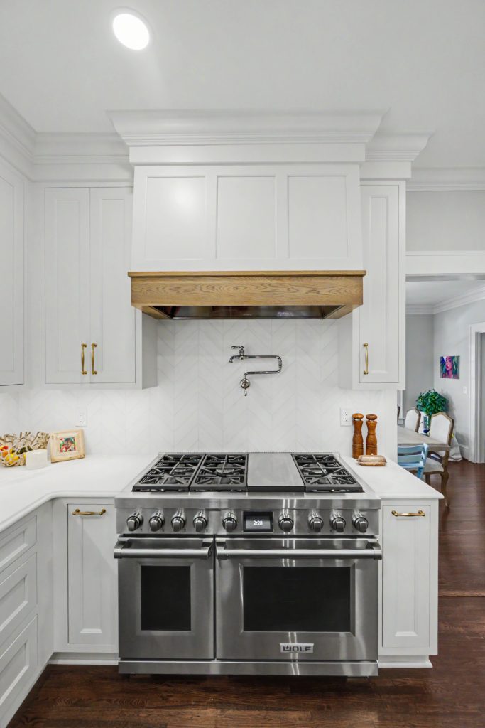 Custom wood range hood above Wolf dual fuel range in white kitchen